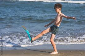 Happy teen boy in the swim flippers having fun on the sand оn the ...